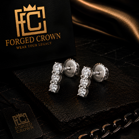 Three stone moissanite drop stud earrings in platinum plated sterling silver with round cut stones and screwback design on a black surface with 'Forged Crown' branding.