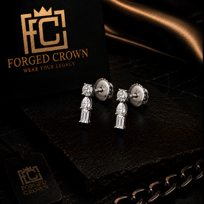 Moissanite 3 Stone Mixed Cut drop stud earrings in platinum plated sterling silver with round, pear and baguette stones in vertical arrangement
 on a black card with 'Forged Crown' branding.
