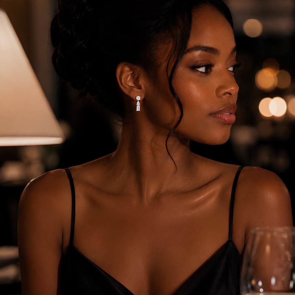 Woman in a black dress wearing moissanite 3 Stone Mixed Cut drop stud earrings in platinum plated sterling silver with round, pear and baguette stones in vertical arrangement