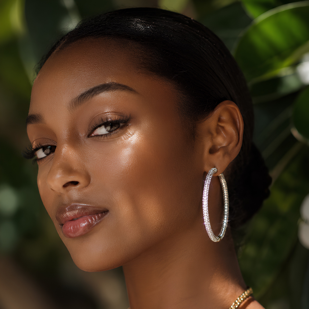 Woman wearing large silver moissanite hoop earrings with continuous pave setting in front of a blurred green background